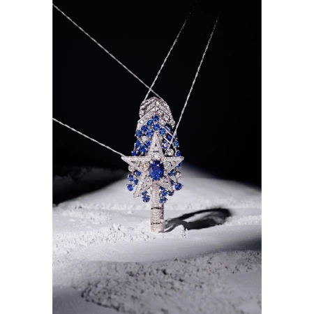 Necklace with blue gemstones in star and drop shapes on a white reflective surface with a dark grey background, studio shot.