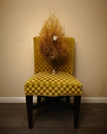 Checkered yellow chair with a silver stand holding a tangle of dry grass and a small white origami flower by Almakarina