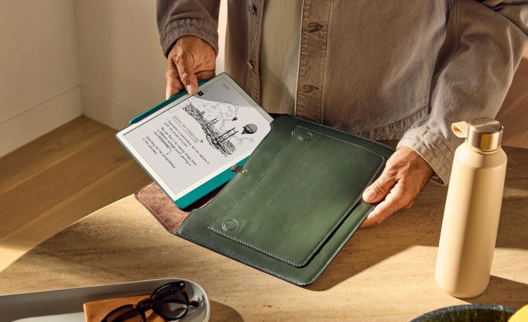 Person holding an open tablet with a drawing on screen and a green folio case on a wood table with a water bottle nearby.