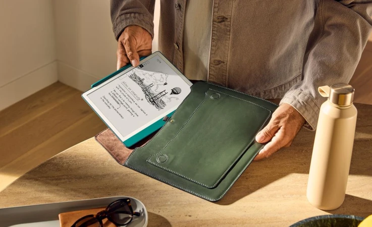 Person holding an open tablet with a drawing on screen and a green folio case on a wood table with a water bottle nearby.