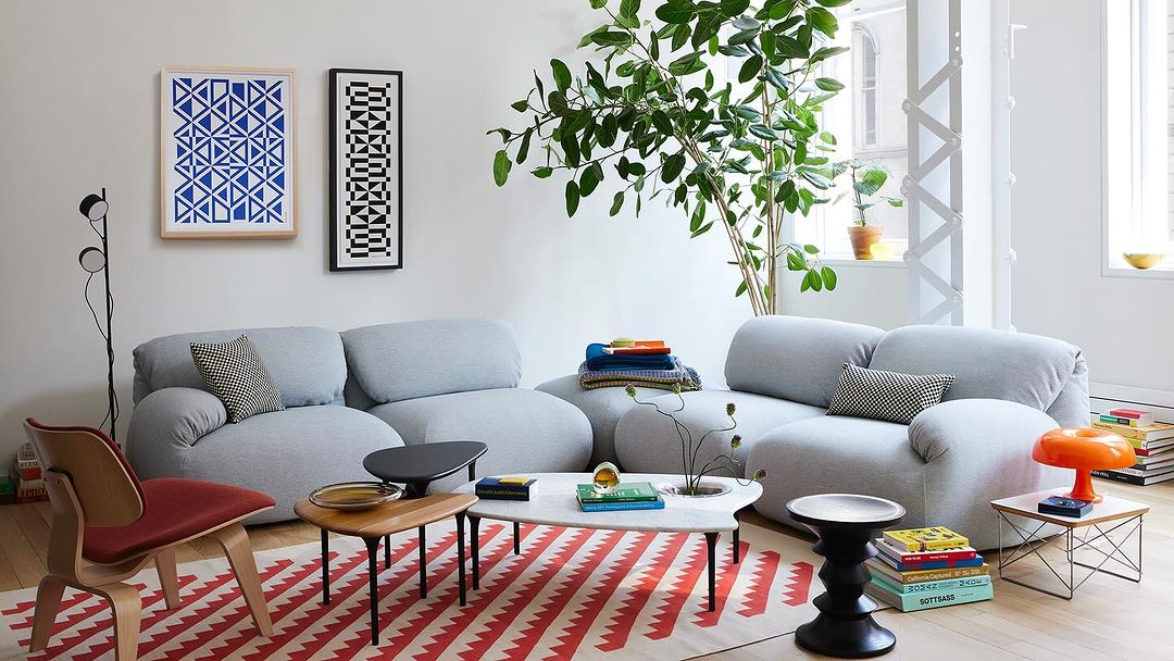 Living room interior featuring a grey sofa, patterned rug, and various decor elements, with a bright and airy ambiance.
