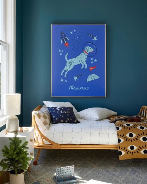 Whimsical kid's room interior with a framed poster of a Dalmatian astronaut, a rattan daybed, and a mini Christmas tree on a side table.