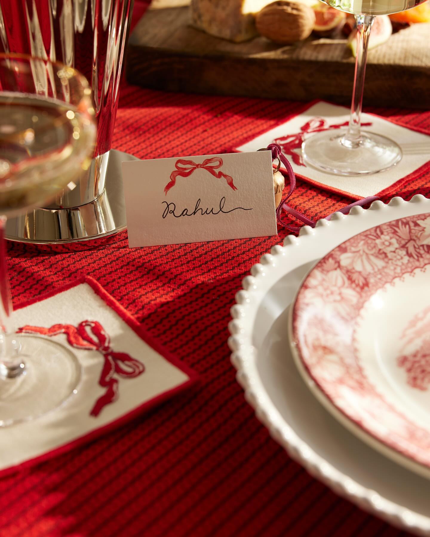 A table setting features a plate, crystal glass, name card with a bow illustration, and a red tablecloth, creating a festive and elegant ambiance.