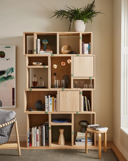 Stacked shelving unit with books, pottery, glassware, and decorative objects on display. Indoor home furnishing with Scandinavian design.