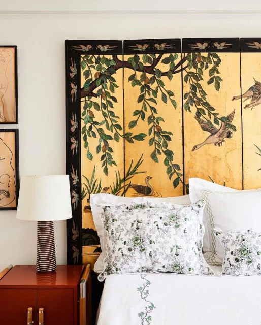 Bedroom interior featuring a bed with white patterned bedding, a decorative screen headboard, red nightstand, and wall art.