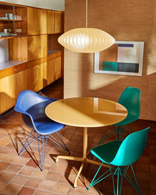 Indoor shot of a round table with three chairs in a dining room setting with wood cabinets, geometric art, and a hanging light fixture.