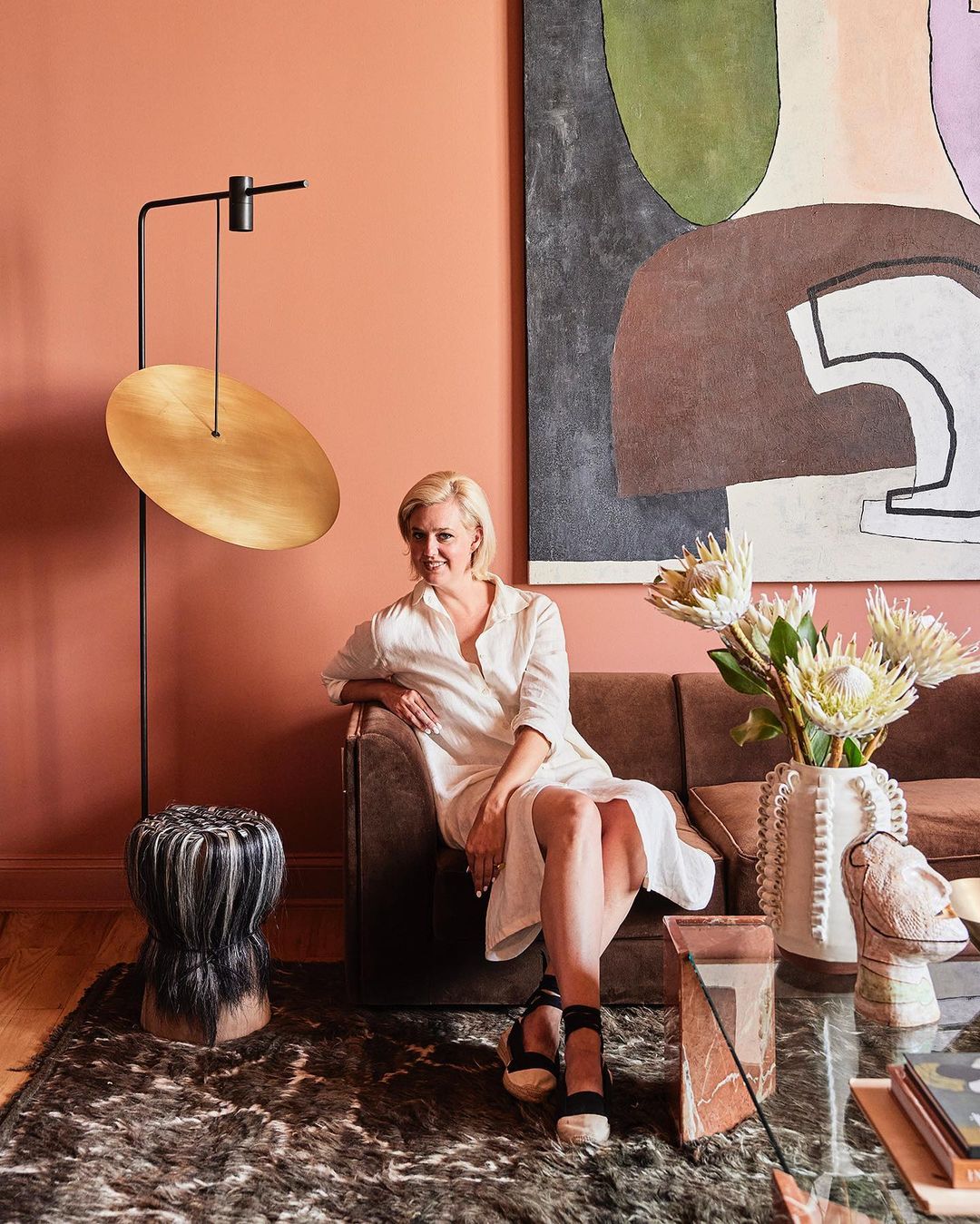 Blonde woman in white shirt dress seated on a brown sofa in a terracotta-walled living room by photographer Alpha Smoot