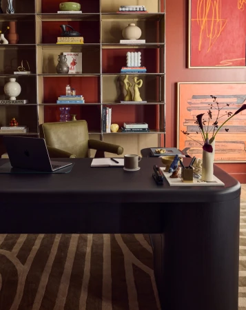 Home office featuring a black desk with a laptop, chair, bookshelf with various objects, and abstract art on the red walls.