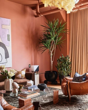 Living room interior with a brown sofa, glass-topped coffee table, potted plants, and a decorative chandelier in an earth-toned color scheme.