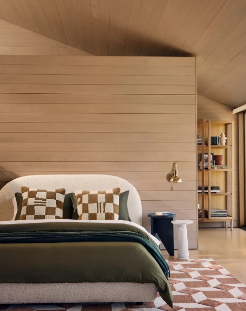 Bedroom interior featuring a bed with olive green bedding, patterned pillows, a wooden paneled wall, and a geometric rug, creating a cozy atmosphere.