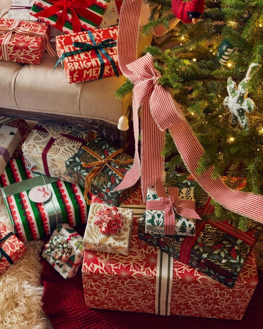 Festive Christmas presents with colorful wrapping and ribbons are arranged beneath a decorated Christmas tree, creating a holiday scene.