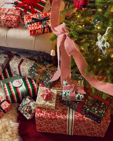 Festive Christmas presents with colorful wrapping and ribbons are arranged beneath a decorated Christmas tree, creating a holiday scene.