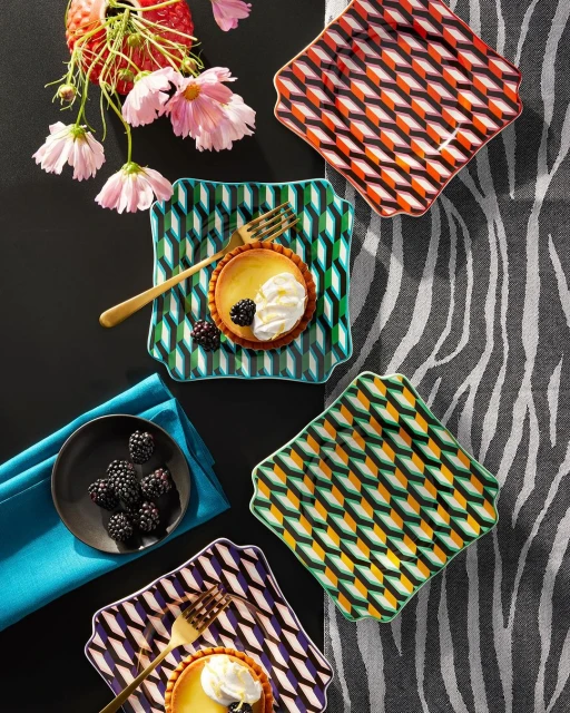 Overhead shot of patterned dessert plates, tarts with cream, blackberries, flowers and a gray zebra-striped background creates elegant food styling.