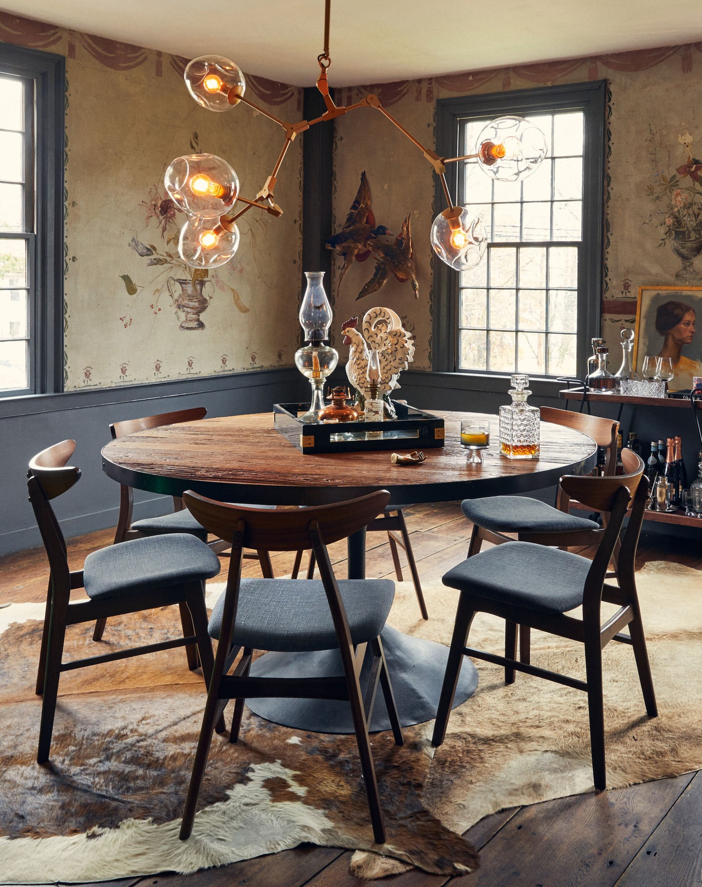Dining room interior featuring a round wooden table, mid-century modern chairs, and a unique chandelier, set on a cowhide rug.
