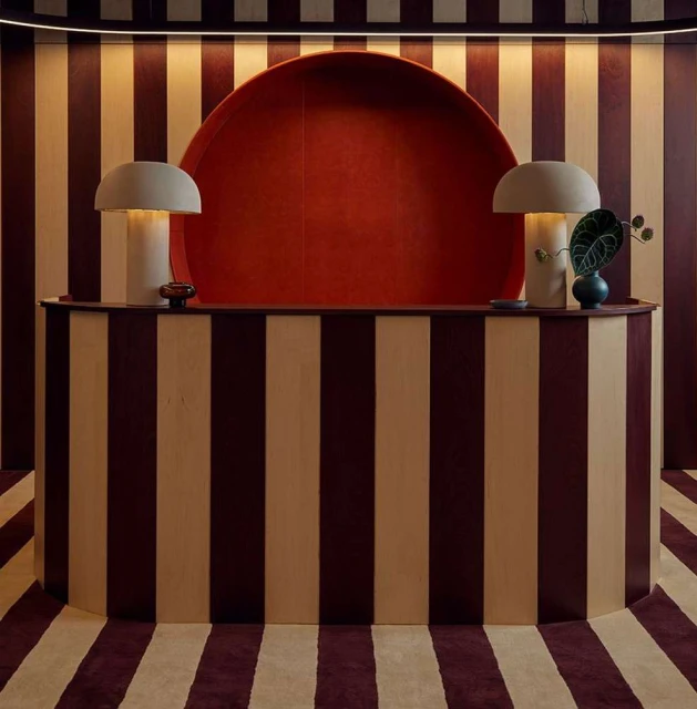 Interior shot of a curved reception desk with striped walls and carpets, illuminated by mushroom lamps, in a photo studio setting.