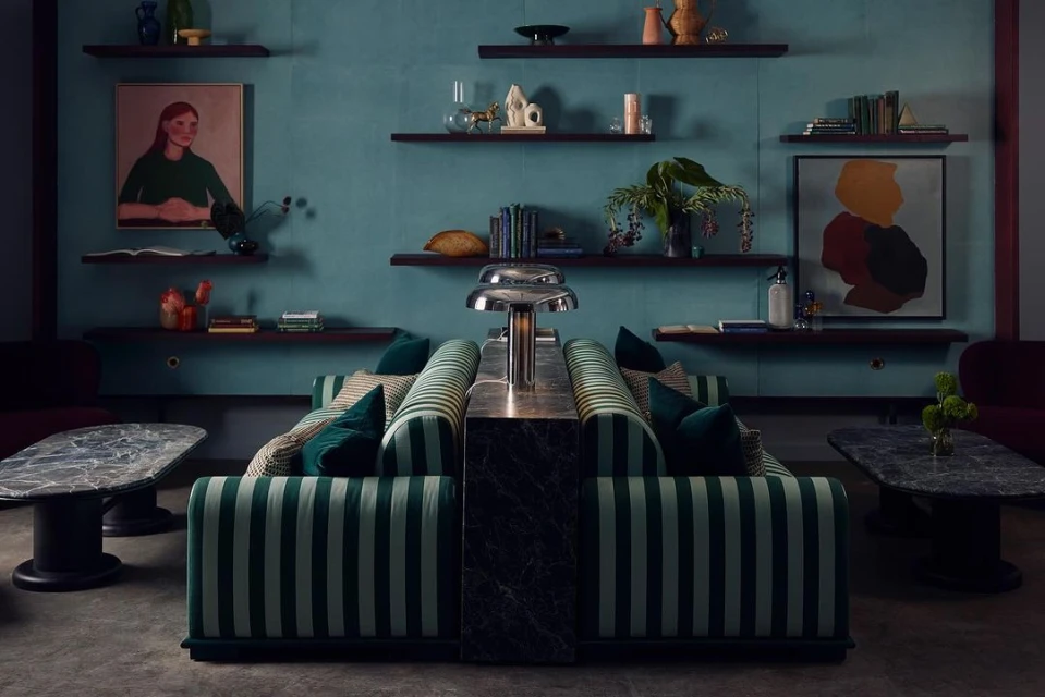 Interior with striped sofas, marble tables, and floating shelves displaying art and decor against a blue textured wall.