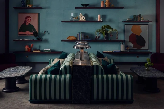 Interior with striped sofas, marble tables, and floating shelves displaying art and decor against a blue textured wall.