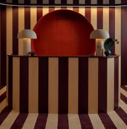 Curved reception desk with vertical burgundy and cream stripes, illuminated lamps, and a large circular red alcove behind it.