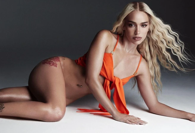 Blonde woman wearing an orange top posing on a grey seamless studio background