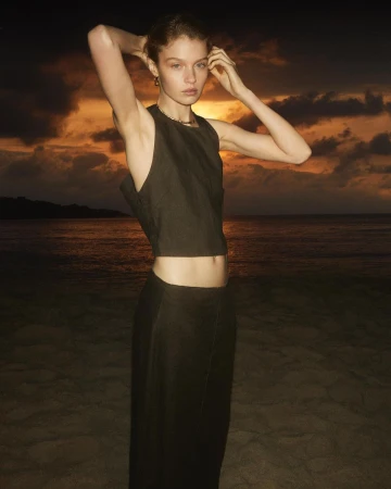 Model in a dark sleeveless crop top and matching skirt posing on a sandy beach at sunset by Alvaro Beamud Cortes