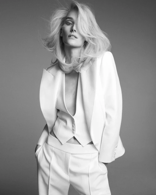 Black and white portrait of a blonde woman wearing a white pantsuit in a photo studio setting with a neutral background, professional fashion look.