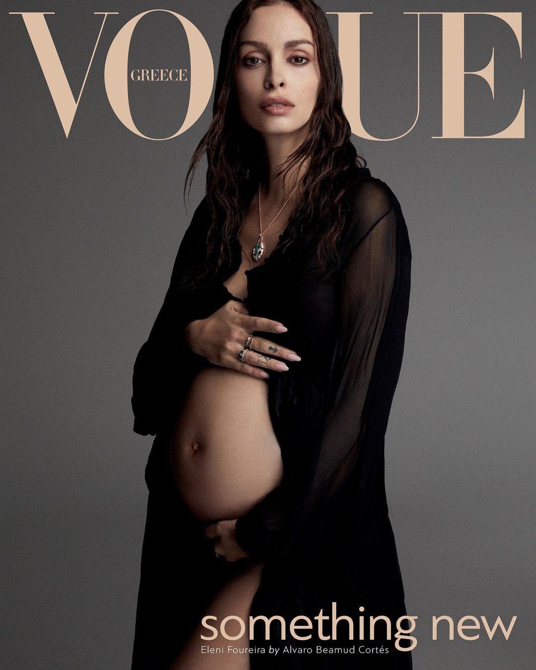 A pregnant woman poses in a sheer black robe for a Vogue Greece cover, against a grey backdrop. She is fair-skinned with brown hair.