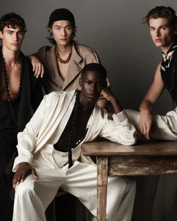 Four male models in stylish attire posed together around a wooden table in a studio setting.
