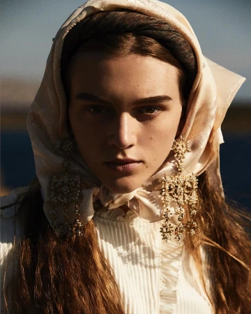 Close-up portrait of a woman wearing a cream silk headscarf and ornate gold statement earrings by photographer Alvaro Beamud Cortes.