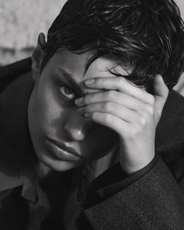 Close-up black and white portrait of a model with wet dark hair holding a hand to their forehead.