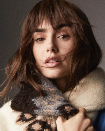 Close-up portrait of a woman with brown hair and bangs wearing a chunky patterned knit scarf and cream sweater.
