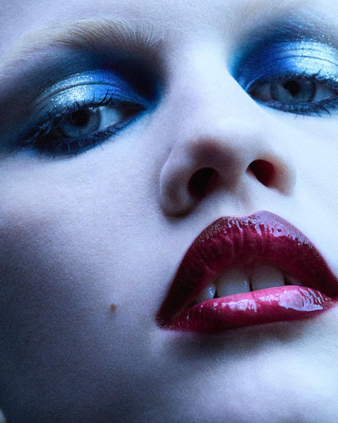 Close-up studio portrait featuring a model with blue eyeshadow and red lipstick, emphasizing makeup artistry and studio beauty photography.