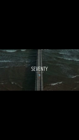 Aerial view captures a solitary figure walking along a narrow pier surrounded by choppy, dark ocean waves, under a dim light.