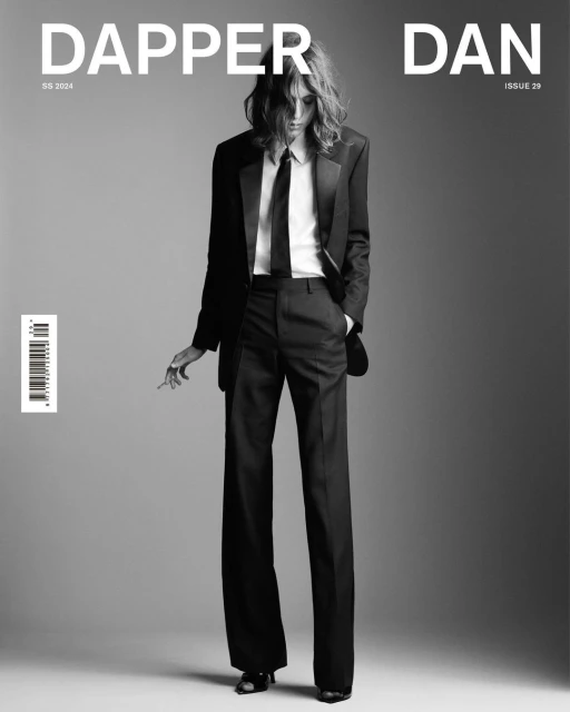 Black and white magazine cover featuring a person in a suit, tie, and long hair, standing against a gray background.