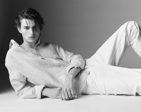 Monochrome portrait of a young male model in a striped shirt and light trousers lying down, photographed by Alvaro Beamud Cortes.