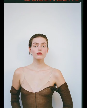 Portrait of a woman wearing a sheer brown top with spaghetti straps against a plain white wall