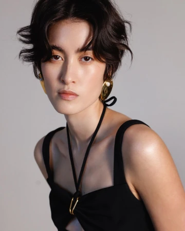 Portrait of a woman with dark short wavy hair wearing a black halter top and large gold earrings by photographer Alvaro Goveia.