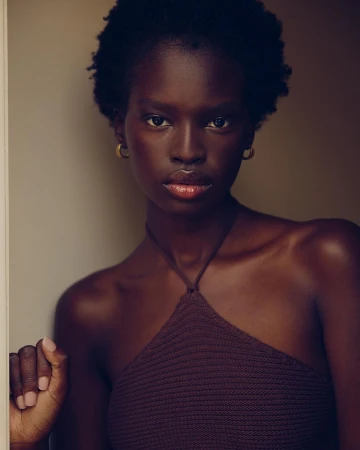 Portrait of a Black woman with short curly hair wearing a brown halter top and gold hoop earrings against a dark background