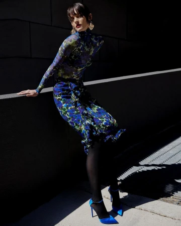 Model in blue floral patterned top and matching skirt leaning against a concrete wall outdoors