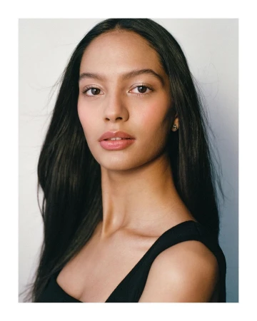 Close-up portrait of a woman with long dark hair wearing a black top against a plain white background by photographer Alvaro Goveia.