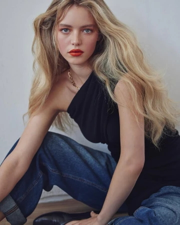 Blonde female model with bold red lips wearing a black one-shoulder top and blue jeans by Alvaro Goveia