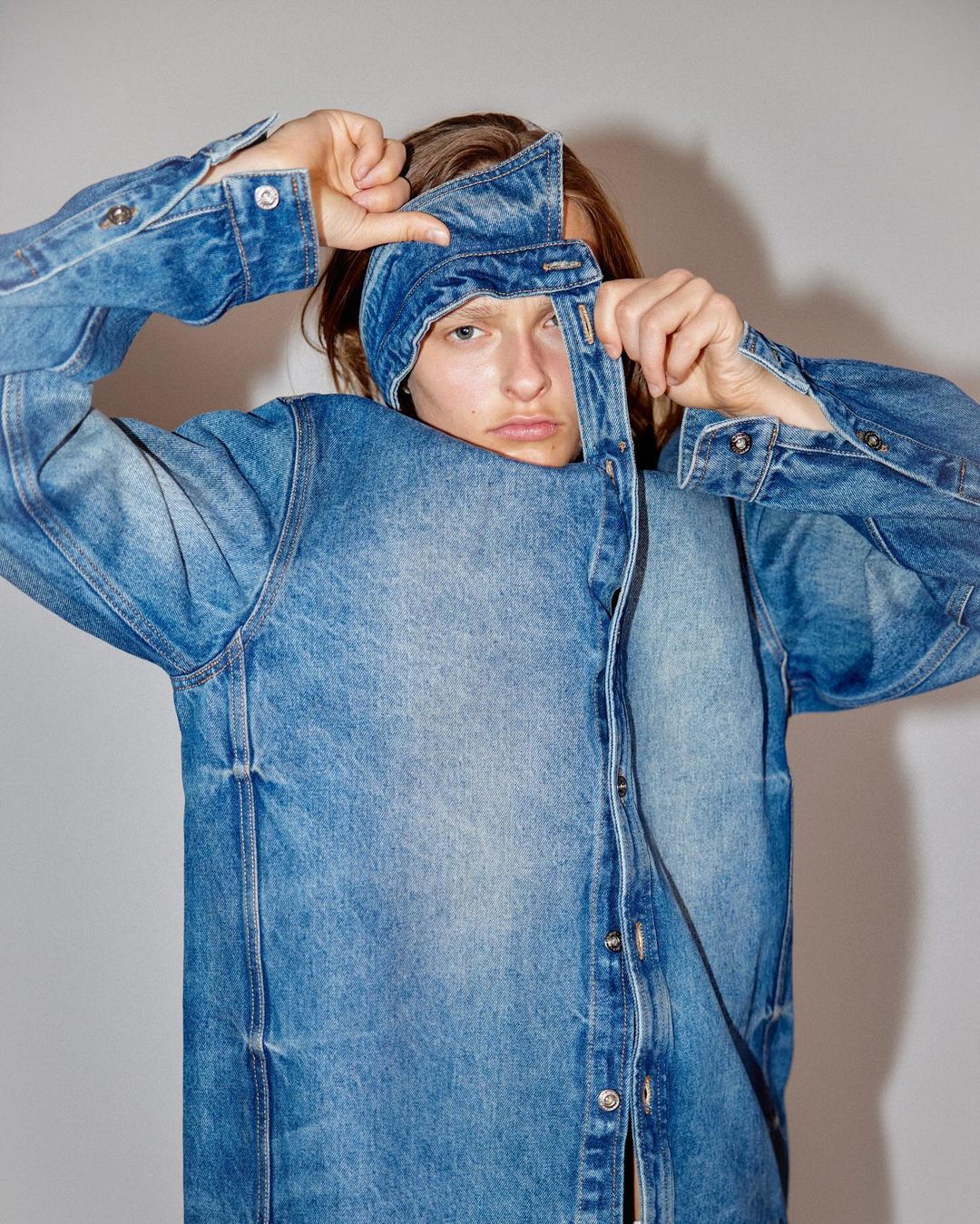 Adult male poses with a denim shirt over his head indoors. The shirt is blue and the background is a plain gray wall.