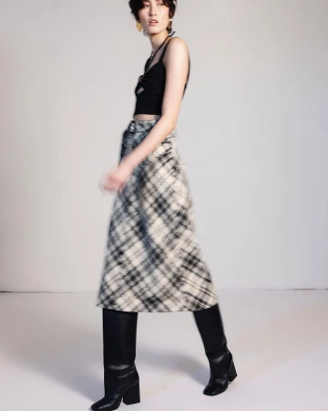 Model wearing a black crop top and plaid midi skirt with black knee-high boots in a studio setting
