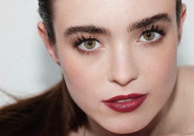 Close-up portrait of a woman with green eyes, dark eyebrows, and deep red lipstick against a plain white background by Alvaro Goveia.