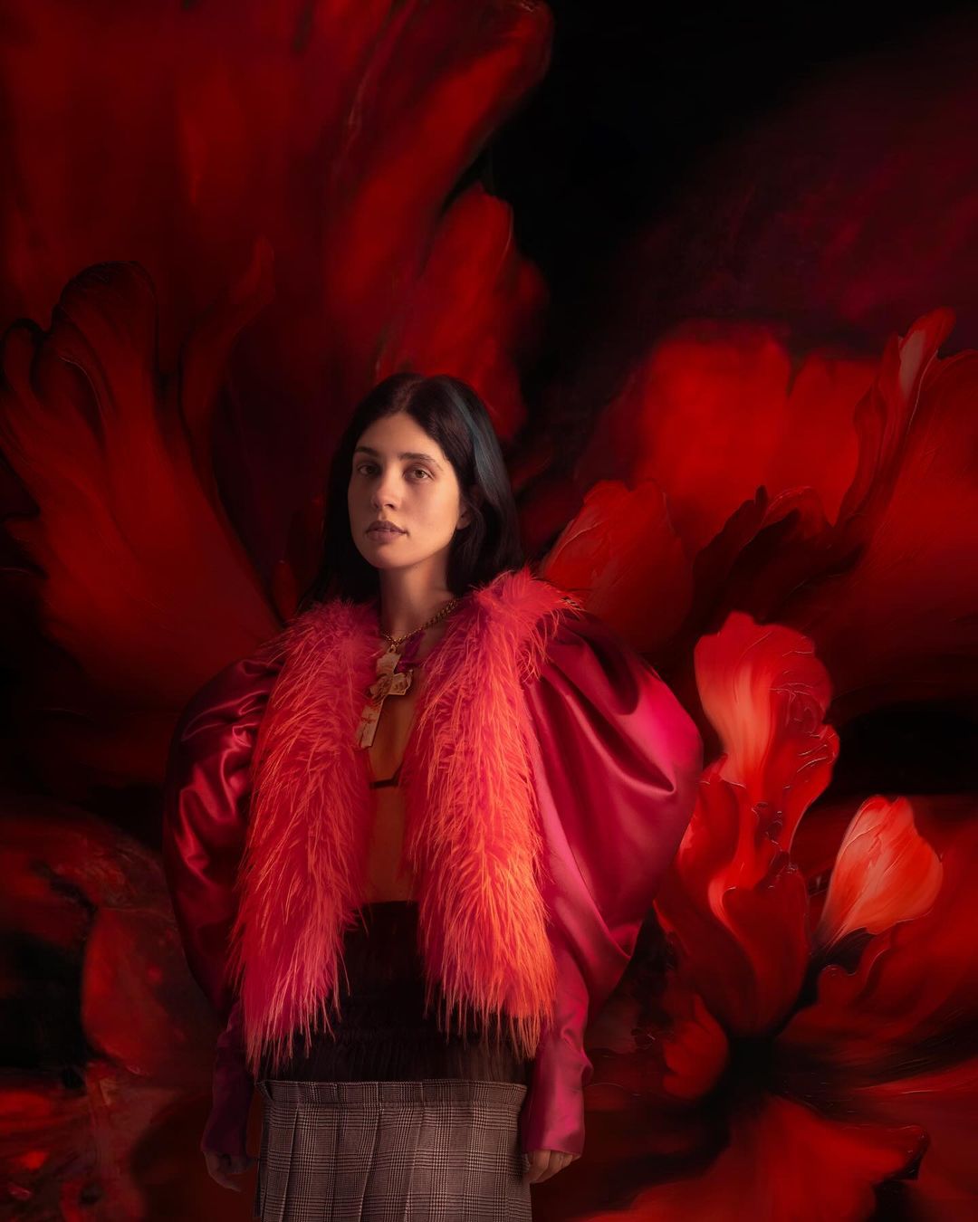 Portrait of a young woman in a pink jacket with a faux fur collar, posing against a red and black floral background.