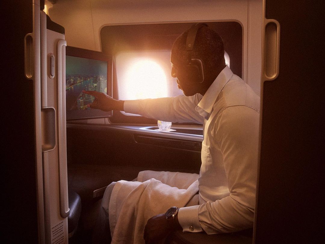 Adult man wearing headphones in an airplane first-class cabin using the entertainment screen during a daytime flight, creating a peaceful travel scene.