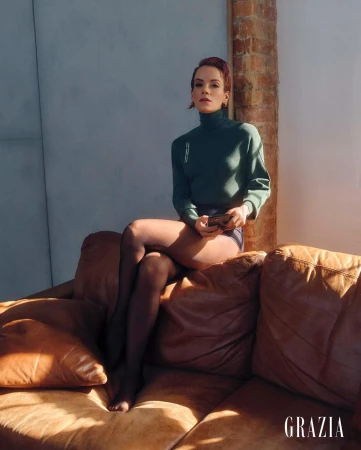 Woman with red hair wearing a dark green turtleneck sweater sitting on a leather sofa by Amanda Fordyce