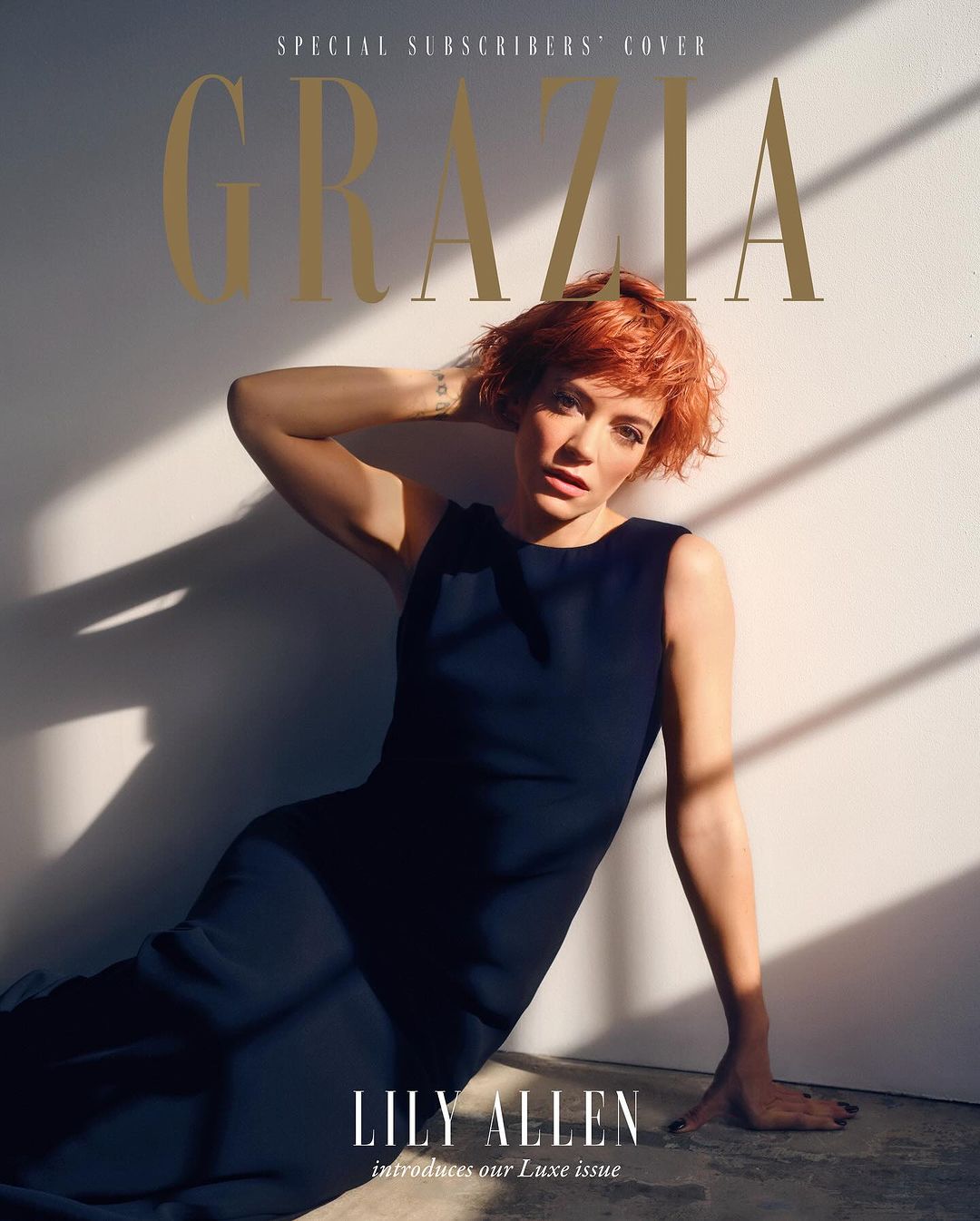 Lily Allen poses in a navy dress for a magazine cover against a light backdrop with shadows creating visual interest and depth.
