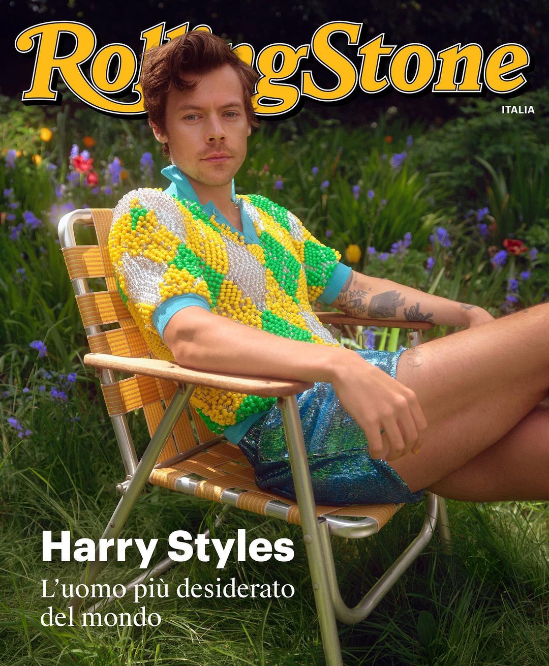 Harry Styles on the cover of Rolling Stone Italia, sitting in a chair outside with green grass and purple flowers in the background.