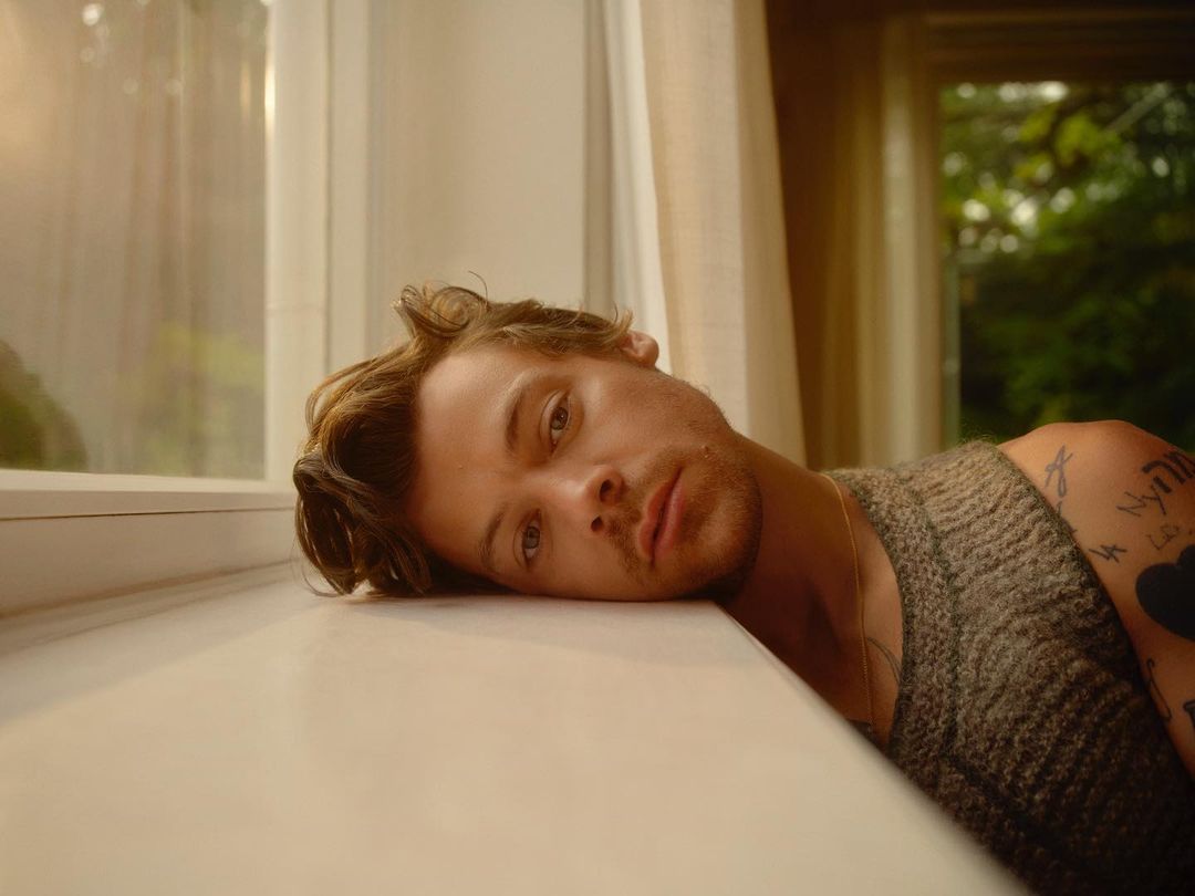 Close-up of a fair-skinned adult male with wavy brown hair lying against a windowsill in an indoor setting, illuminated by natural light.