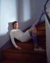 Harry Styles seated on wooden stairs wearing floral patterned tights and white t-shirt by photographer Amanda Fordyce